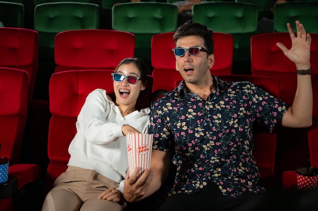 Photo in a cinema a young couple pair wearing 3d glasses watches movies and eats popcorn