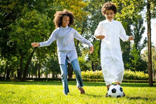 Cinematic image of a family from the emirates spending time at the park. Brother and sister playing soccer in the grass