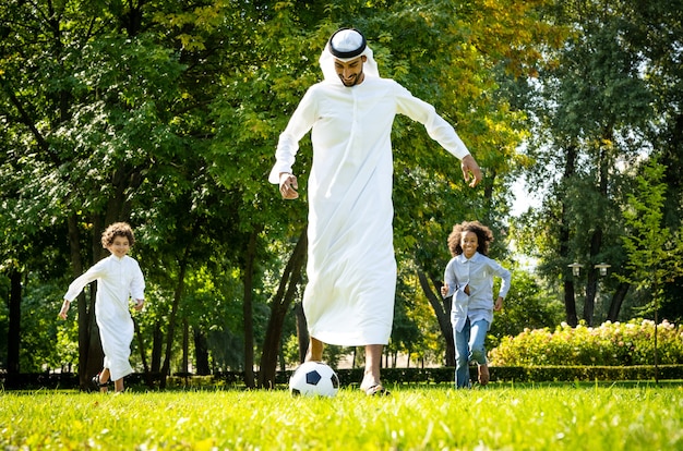 Cinematic image of a family from the emirates spending time at the park. Brother and sister playing soccer in the grass