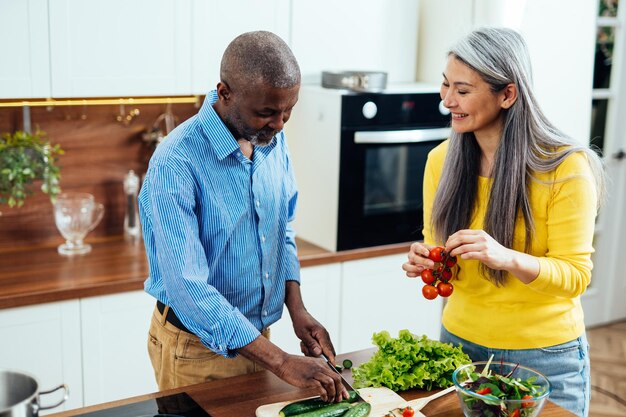 Cinematic image of a multiethnic senior couple preparing food in the kitchen Indoors Lifestyle moments at home Concept about seniority and relationships