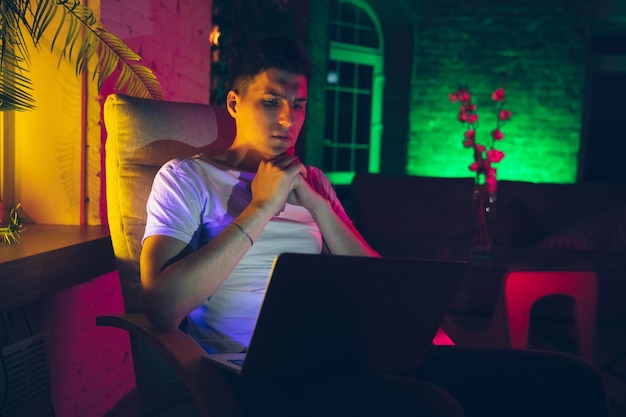 Photo cinematic portrait of handsome young man using devices gadgets in neon lighted interior
