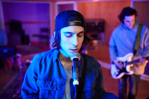 Cinematic portrait of young man singing with eyes closed in colored studio lights copy space