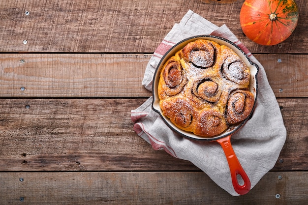 Cinnabon kaneelbroodjes broodjes met pompoen, noten, karamel en suikerroom bevroren op rustieke houten achtergrond. Bovenaanzicht. Zoete zelfgemaakte gebak kerst bakken. Kanelbule - Zweeds dessert.