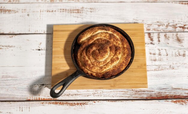 Cinnamon bun in black metal pan on the wooden table