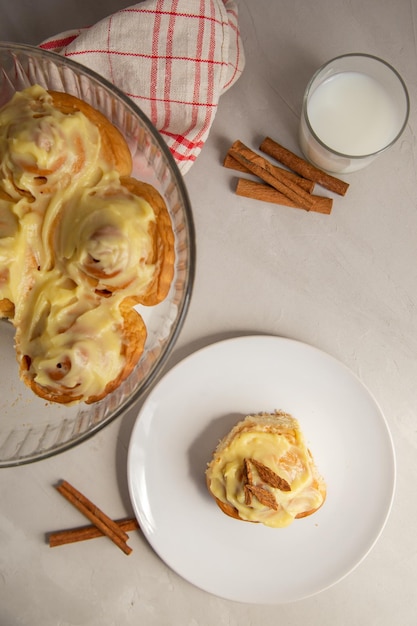 Panino alla cannella con glassa e bastoncini di cannella con un bicchiere di latte su uno sfondo grigio chiaro vista dall'alto