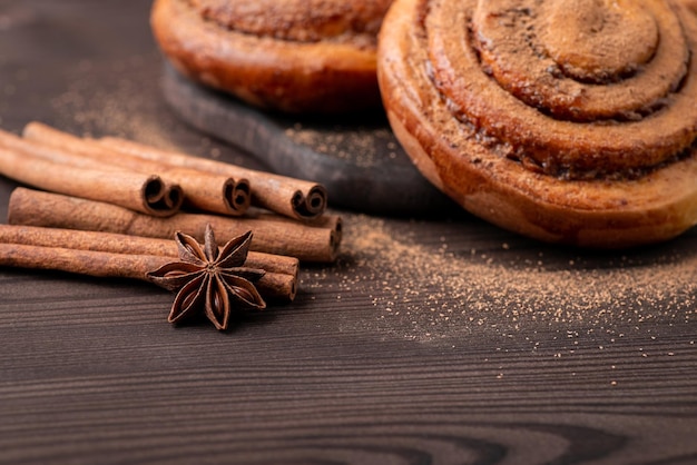 Foto panini alla cannella sul tavolo di legno nero. bastoncini di cannella e stelle di anice vicino ai panini