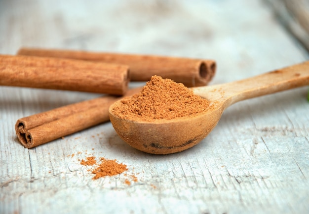 Cinnamon powder in a wooden spoon next to cinnamon sticks.