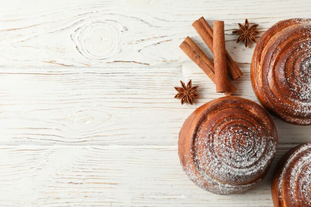 Cinnamon rolls with powdered sugar and cinnamon sticks on white wooden