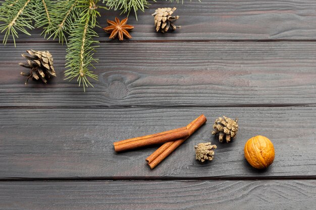 Cinnamon sticks and nuts. Pine branches and cones on dark wooden background. Copy space. Flat lay