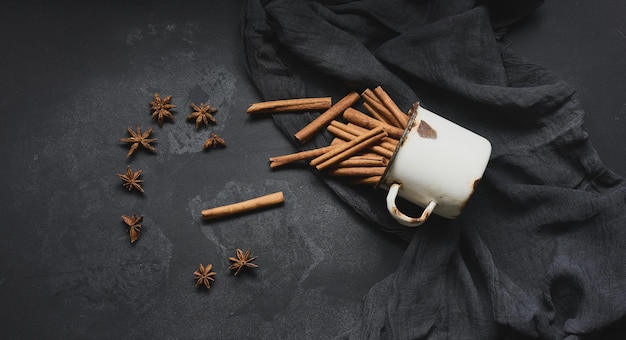 Photo cinnamon sticks in an old metal mug on a black table. aromatic spice