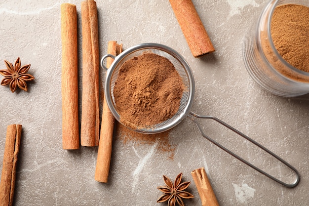 Photo cinnamon sticks, powder and sieve on grey wall, top view