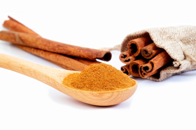 Cinnamon sticks and powder in wooden spoon isolated on white