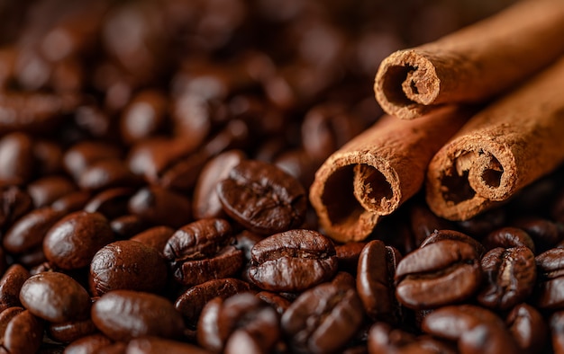 Cinnamon sticks on roasted coffee beans background. Copy space, close up.