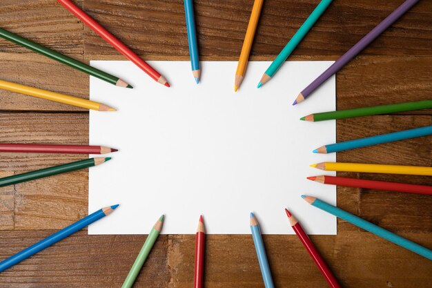 Photo a circle of colored pencils with a blank white paper in the middle.