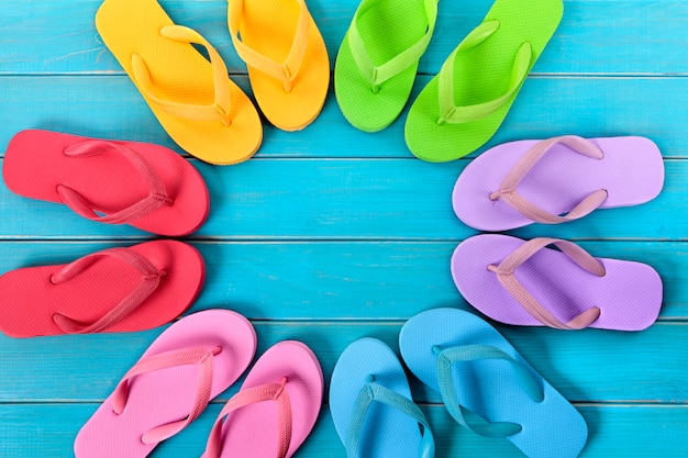 Circle of colorful flip flops on old weathered blue painted beach decking.  