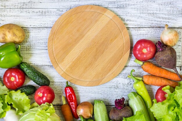 白い木製の背景にサークルまな板と野菜健康的な食事