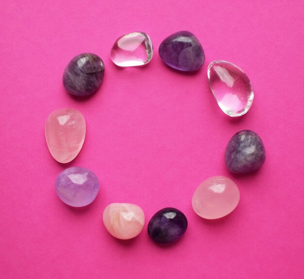 Photo the circle is lined with natural minerals. semi-precious stones of different colors processed. amethyst and rose quartz. frame of gems on bright pink background.