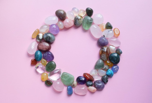 Photo the circle is lined with natural minerals semiprecious stones of different colors raw and processed amethyst rose quartz agate apatite aventurine on a pink background