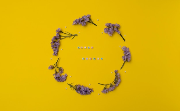 Circle made of purple lavender flowers with white beads on yellow background spring summer concept