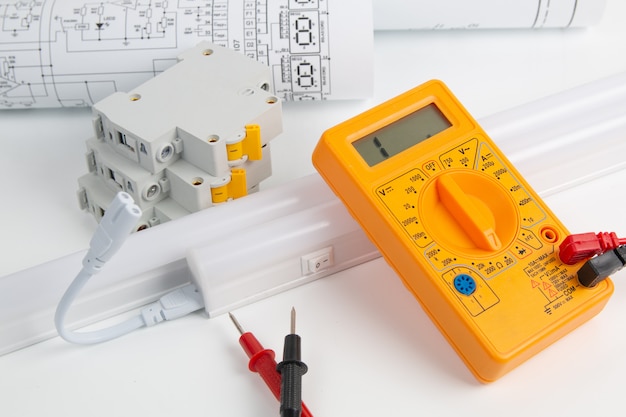 Circuit breaker, drawings, LED lamp and digital multimiter on white table