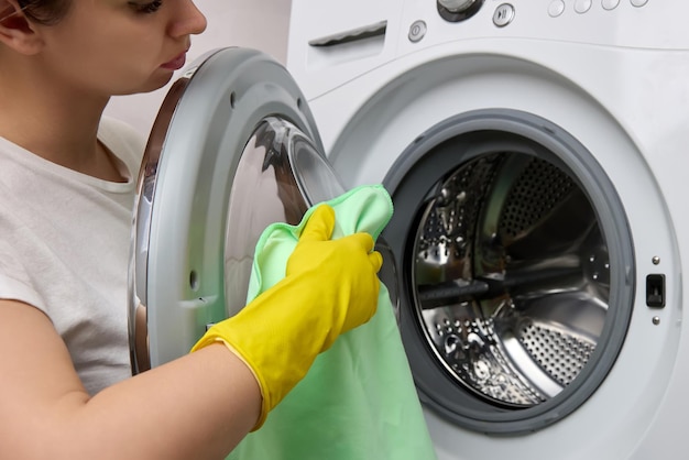 Circular motion girl in yellow protective gloves wipes door washing machine dry