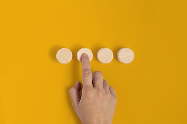 The circular wooden block is placed on a yellow background and the hand gestures press against the wooden block similar to pressing a button. banner with copy space for text, poster, mockup template.