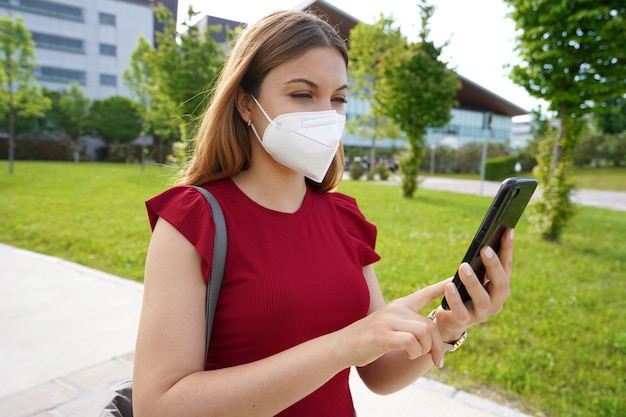 屋外で彼女の携帯電話を見ている医療マスクを持つ市民の女性。グリーンパスとデジタルcovid証明書の概念。