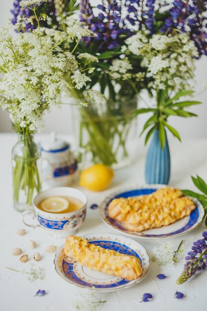 Citroeneclairs en citroenthee in een vintage theeservies en bloemen op wit