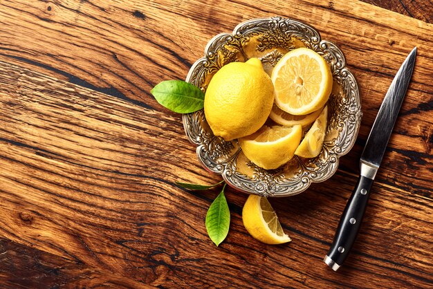 Foto citroenen met bladeren op eiken houten tafel. kopieer ruimte voor ontwerp of tekst. bovenaanzicht van fruit met mes.