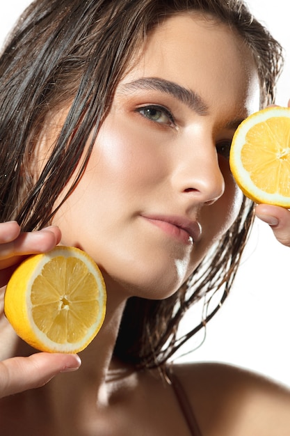 감귤류는 흰색 배경 화장품 위에 레몬 조각을 얹은 아름다운 여성의 얼굴을 닫습니다.