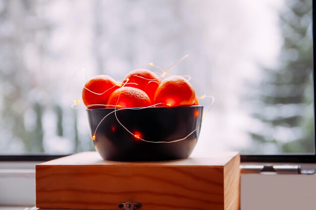 Citrus fruits in a black ceramic cup on a window background Still life on a winter day
