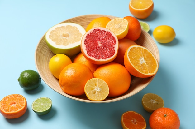 Citrus fruits and bowl on light blue background, close up