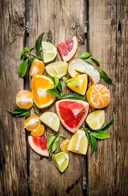 柑橘系の果物-グレープフルーツ、オレンジ、みかん、レモン、ライムをスライスし、葉で丸ごと。木製のテーブルの上。上面図