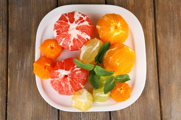 Citrus fruits without skin, on plate, on wooden background