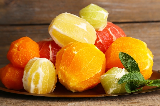 Citrus fruits without skin on tray, on wooden background