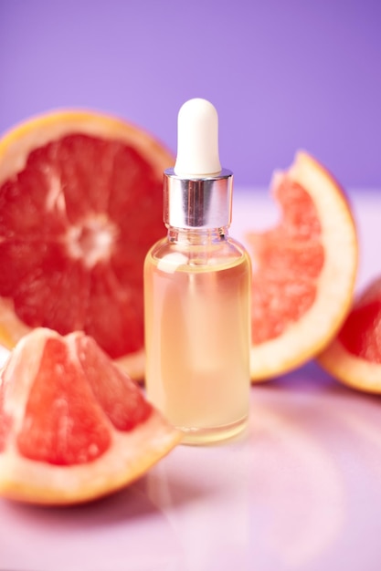 Citrus or grapefruit essential oil in glass bottle with fresh grapefruit on trendy purple background Spa and skincare product