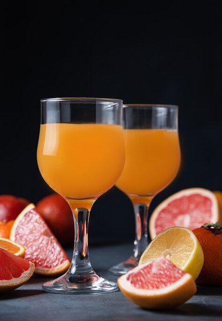 Citrus juice in two glasses and fresh fruit tangerine, orange, grapefruit and lemon on a black background. Front view