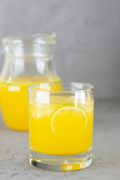 Цитрусовый сок с ломтиками лайма в стакане и кувшин на сером фоне