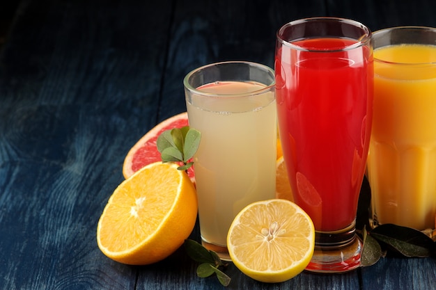 柑橘系のジュース。青い木製のテーブルに新鮮な果物とオレンジ、グレープフルーツ、レモンジュース。テキスト用のスペース