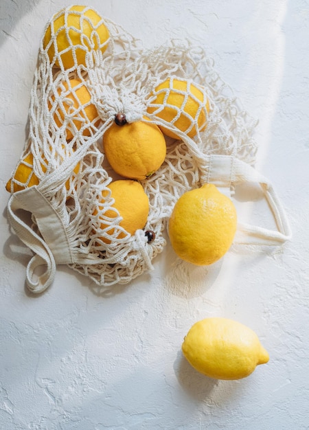 白い背景の上面図に枝編み細工品の綿袋ストリング バッグに入ったシトラス レモン