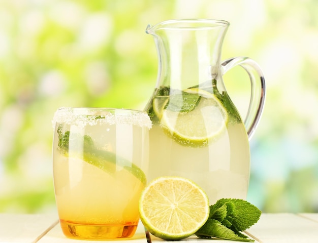 Citrus lemonade in pitcher and glass on wooden table on natural background