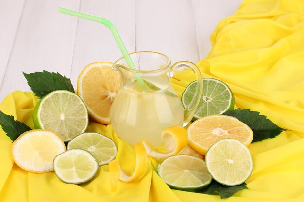 Citrus limonade in glazen kruik van citrus rond op gele stof op witte houten tafel close-up