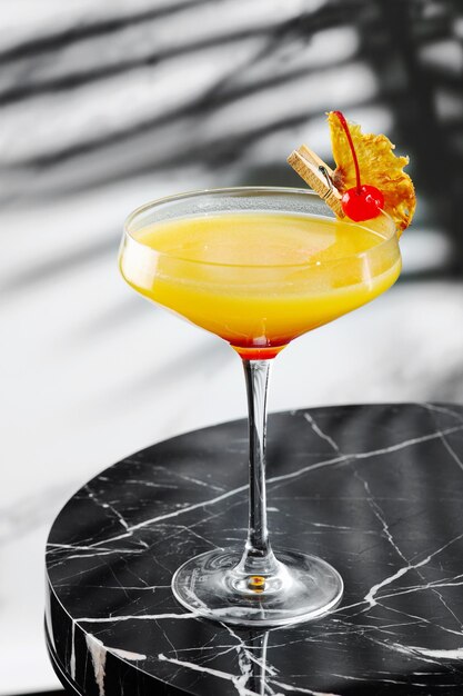 Citrus and pineapple cocktail on marble table close up. tropical cocktail with shadow of tropical plants branch on background