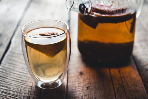 Photo citrus tea in a transparent teapot and a glass, healthy drink on a wooden background.