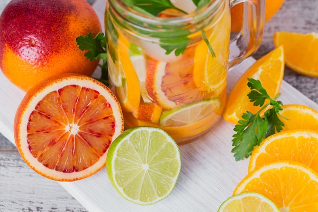 Citrusvruchten en kruidenwater voor detox of dieet in glazen flessen op een houten bord