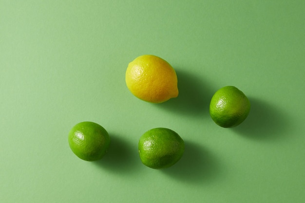 Citrusvruchten op een groene achtergrond. Bovenaanzicht van een groep groene limoenen en een gele citroen.