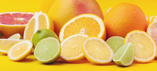 Citrusvruchten (sinaasappel, citroen, grapefruit, limoen) op geel.
