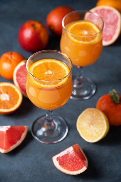 Citrusvruchtensap in twee glazen en vers fruit mandarijn, sinaasappel, grapefruit en citroen op een donkergrijze achtergrond. bovenaanzicht