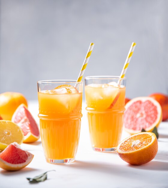 Citrusvruchtensap in twee glazen en vers fruitmandarijn, sinaasappel, grapefruit en citroen op een grijze achtergrond