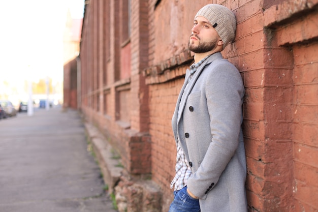 Городской жизни. Стильный молодой человек в сером пальто и шляпе стоит на улице в городе.